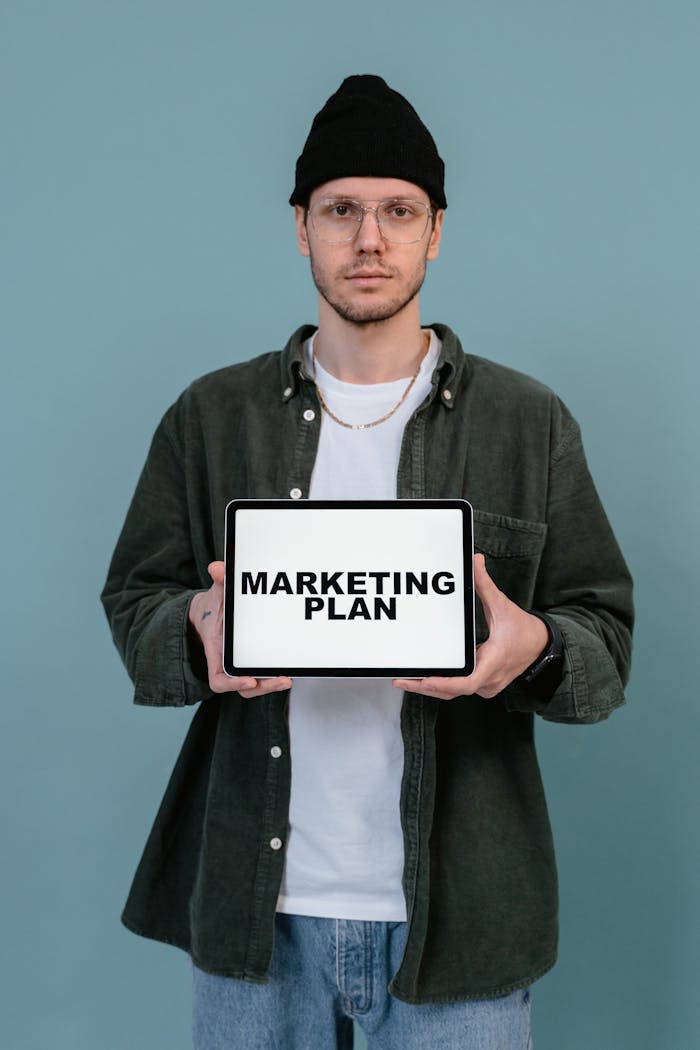 A man in casual attire displays a tablet with 'Marketing Plan' text against a blue background.